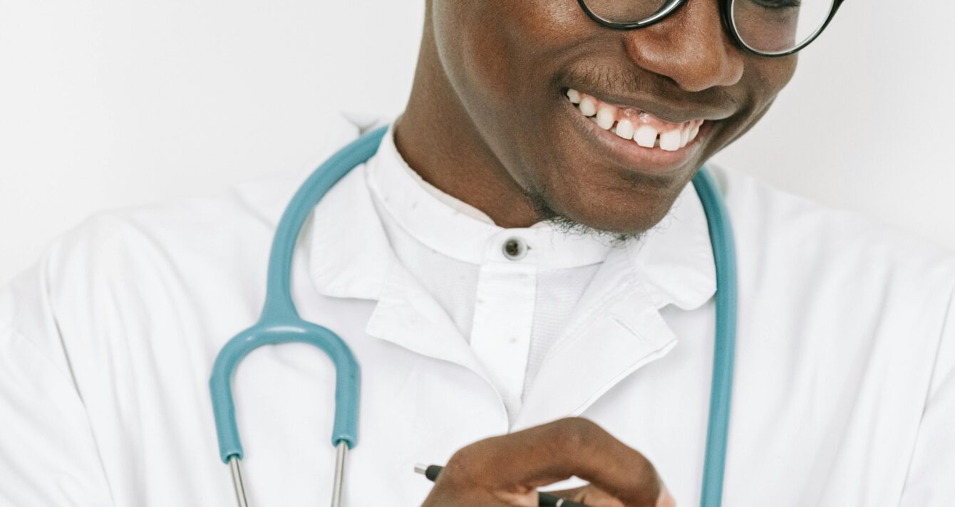 Friendly doctor with stethoscope writing on a chart in a bright room.