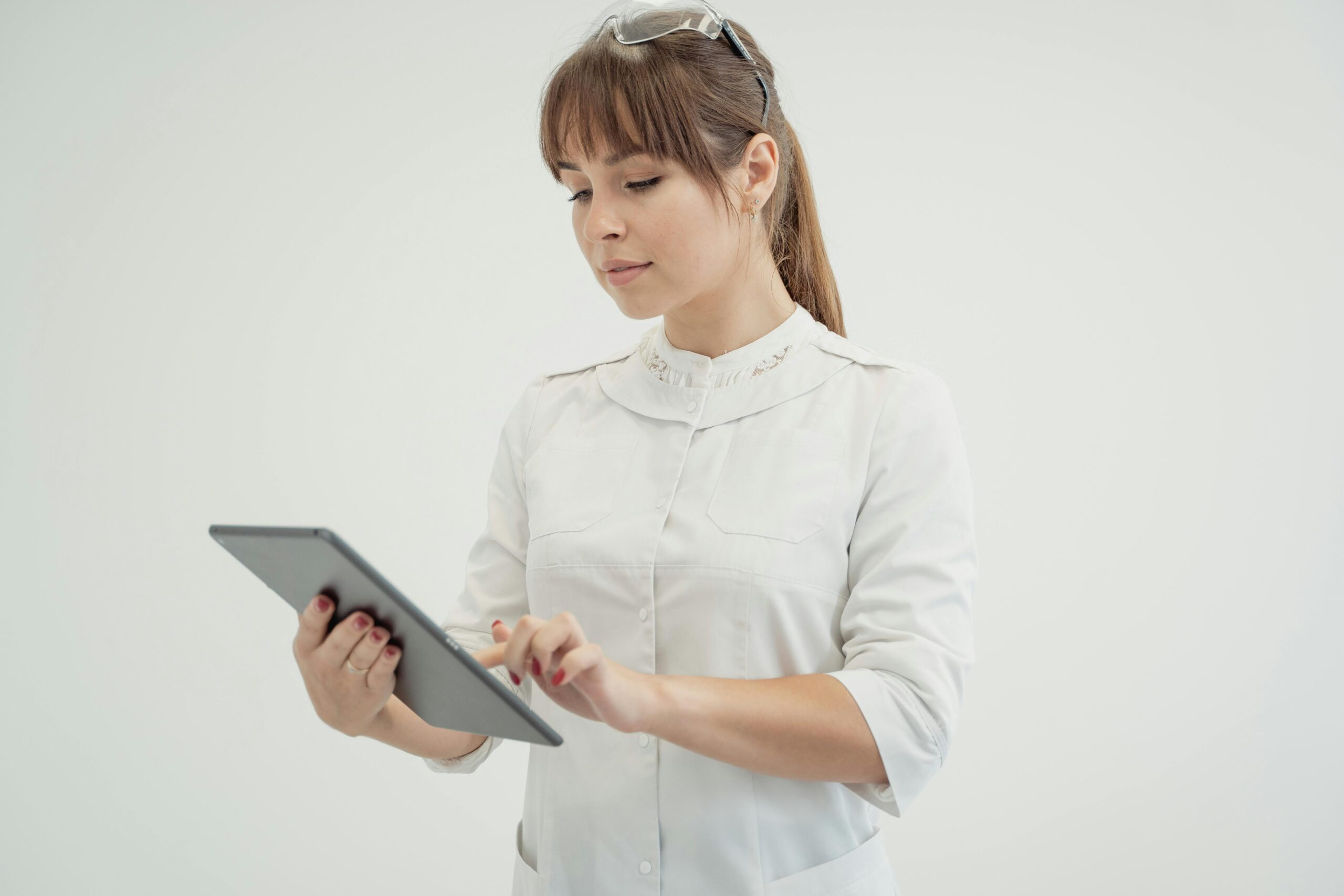 Woman in white uniform using a tablet device, representing modern healthcare technology.